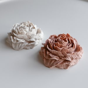 Pode incluir: Duas esculturas de flores decorativas, uma de cor bege claro e a outra de cor rosa claro. As esculturas são feitas de um material texturizado e têm uma forma de flor realista.