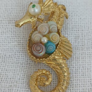 May include: A gold-tone seahorse brooch with a pearl eye and a nest of colorful seashells.