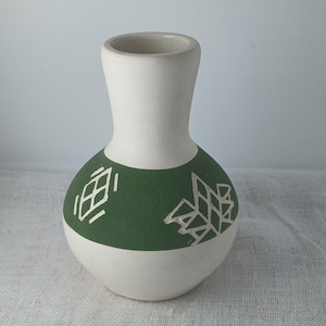 May include: A white ceramic vase with a green band and white geometric designs. The vase has a rounded body and a narrow neck.