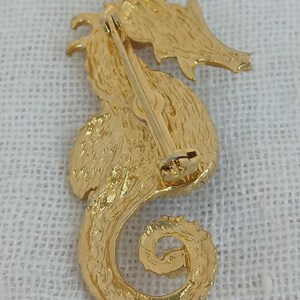 May include: Gold-toned seahorse brooch with a textured finish. The brooch has a pin and catch closure on the back.