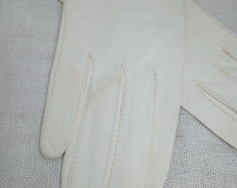 May include: A pair of off-white leather gloves. The gloves have a classic design with stitched seams and a decorative edge. The gloves are likely for formal wear or cold weather.