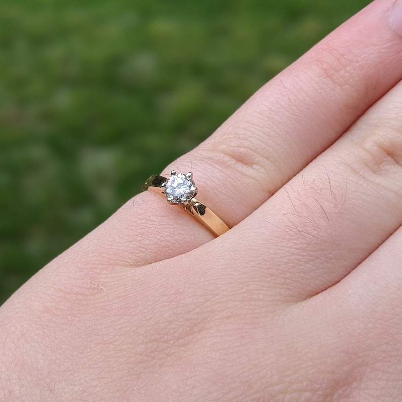 K&ouml;nnte beinhalten: Ein Goldring mit einem einzigen, runden, klaren Diamanten.