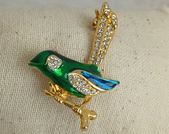 May include: A gold-tone brooch in the shape of a bird with green and blue enamel and clear rhinestones.