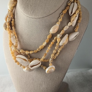 May include: A multi-strand necklace made of small, light brown seashells with larger, white seashells interspersed throughout.