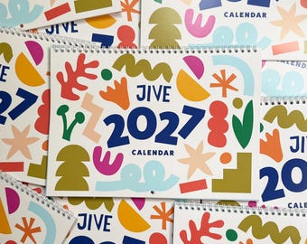 May include: A spiral-bound 2027 Jive calendar featuring a white background with a colorful pattern of abstract shapes in red, orange, yellow, green, blue, and pink. The text JIVE 2027 CALENDAR is printed in large dark blue letters.
