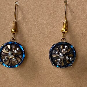 Puede incluir: Un par de pendientes azules y dorados con un diseño de flor y pedrería.
