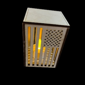 May include: A wooden lantern with a cutout of the American flag and a lit candle inside.