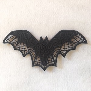 May include: Black lace bat applique with a rose design. The bat is intricately detailed with a web pattern.