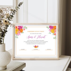 Peut inclure: Un certificat encadré avec des motifs floraux. Le texte indique "CERTIFICAT D'UNION" et comprend des noms et une date. Le certificat est dans un cadre en bois clair, posé sur une surface blanche avec un vase de fleurs et des livres en arrière-plan.