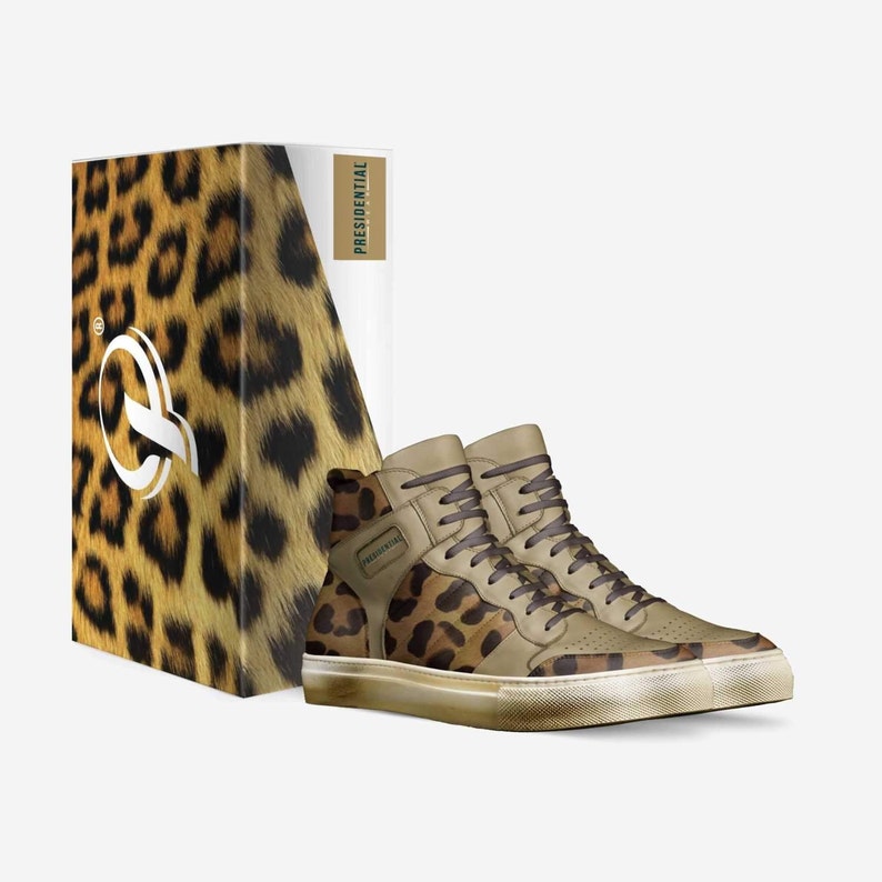 May include: A pair of high-top sneakers with a leopard print design. The shoes have a brown leather upper with a white sole and a green "PRESIDENTIAL" logo on the side. The shoes are packaged in a box with a leopard print design and the word "PRESIDENTIAL" printed on the side.
