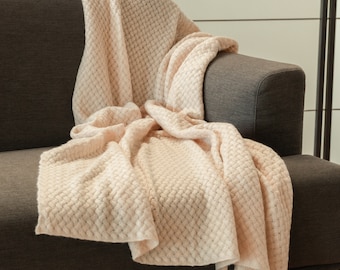 Könnte beinhalten: Eine weiche, cremefarbene gestrickte Wolldecke, die über ein braunes Sofa gelegt ist. Die Decke hat ein strukturiertes, waffelartiges Muster.