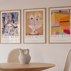 Op de afbeelding: Drie ingelijste kunstprints met abstracte geometrische ontwerpen van Paul Klee. De prints zijn in een licht houten lijst en hebben een witte achtergrond. De prints zijn getiteld "Revolving Rotator", "Retrospective" en "The Twittering Machine".