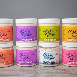 May include: Six jars of whipped lotion with different scents. The jars are labeled "All That Bar of Soap" and have a variety of colors, including pink, purple, orange, yellow, and green.