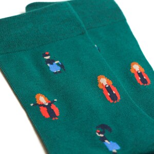 May include: A pair of green socks with a repeating pattern of women in different outfits. The women are wearing red, blue, and black clothing.