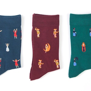 May include: Three pairs of socks with different colorful patterns. The socks are all crew length and feature a variety of designs, including dancing figures, a crescent moon, and a woman in a red dress.