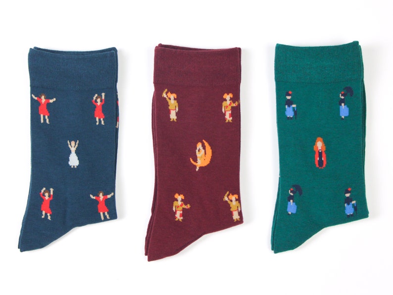 May include: Three pairs of socks with different colorful patterns. The socks are all crew length and feature a variety of designs, including dancing figures, a crescent moon, and a woman in a red dress.