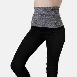 May include: A gray and black waist shaper is worn over black jeans. The waist shaper is a wide band of stretchy material. The jeans are a dark black color.