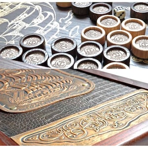 Könnte beinhalten: Ein Holzspielbrett mit nautischem Thema. Das Brett zeigt ein Schiffsdesign und eine lederartige Oberfläche. Die Spielsteine sind aus Holz und haben ein Ankerdesign. Das Spiel heißt "The Seafarers' Game".