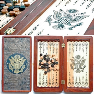 Könnte beinhalten: Ein Backgammon-Set aus Holz mit braunem Lederbezug und einem goldenen Adlerwappen. Das Set ist geöffnet und zeigt die Spielfläche mit schwarzen und braunen Spielsteinen und einem weißen Würfel.