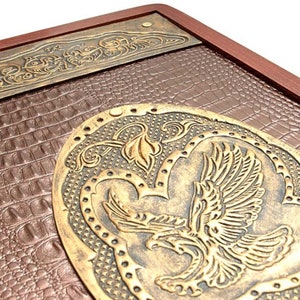 Könnte beinhalten: Eine braune Lederbox mit einem goldenen Adlerdesign und filigranen Blumenmustern. Die Box hat einen Holzrahmen und eine strukturierte Lederoberfläche.