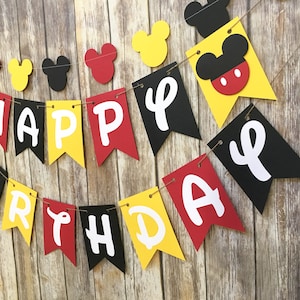 May include: A black, yellow, and red banner with the words "Happy Birthday" in white letters. The banner is decorated with Mickey Mouse ears and heads.