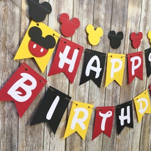 May include: A red, yellow, and black banner with the words "Happy Birthday" in white letters. The banner is decorated with Mickey Mouse heads.