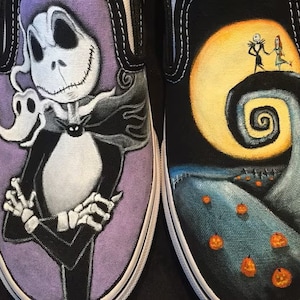 Op de afbeelding: Een paar op maat geverfde Vans slip-on schoenen met personages uit de film The Nightmare Before Christmas. De ene schoen heeft Jack Skellington, de Pumpkin King, op een paarse achtergrond. De andere schoen heeft Jack en Sally op een heuvel met een volle maan en een spiraalvormige heuvel op de achtergrond.