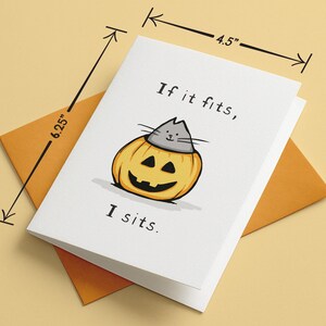 May include: A white greeting card featuring a cartoon illustration of a grey cat sitting inside a yellow jack-o'-lantern pumpkin. The text reads "If it fits, I sits." The card measures 4.5 inches by 6.25 inches and is paired with an orange envelope.