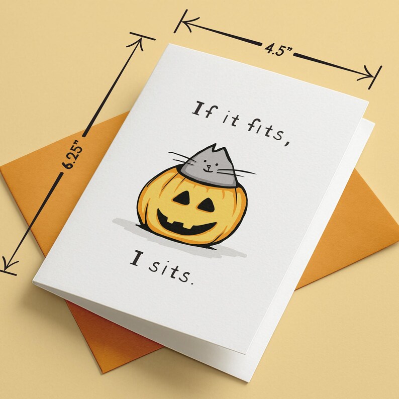 May include: A white greeting card featuring a cartoon illustration of a grey cat sitting inside a yellow jack-o'-lantern pumpkin. The text reads "If it fits, I sits." The card measures 4.5 inches by 6.25 inches and is paired with an orange envelope.