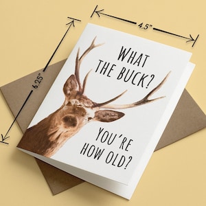 May include: A white greeting card featuring a brown deer with antlers and the black text WHAT THE BUCK? YOU'RE HOW OLD? The card measures 4.5 inches by 6.25 inches and is placed on top of a brown envelope.