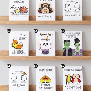 May include: A collection of nine rectangular greeting cards featuring cartoon illustrations and puns for Halloween. Each card displays unique characters like ghosts, candy corn, and food items with text captions, arranged in three rows on wooden shelves.