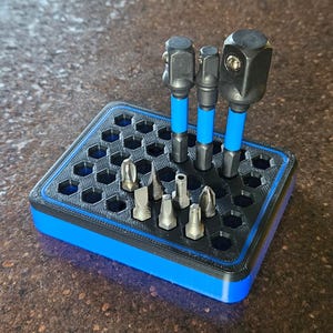 May include: A blue and black tool organizer with various metal bits and three black impact sockets with blue accents. The organizer has a honeycomb pattern and is designed to hold different types of tools.