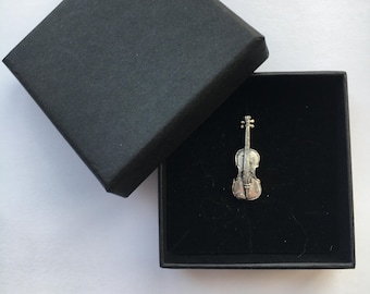 May include: A silver violin pin in a black velvet box. The pin is a detailed representation of a violin.