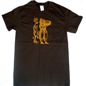 May include: A brown t-shirt featuring a gold-coloured illustration of a person carrying a barrel and a vine with grapes. The illustration is in a vintage style.