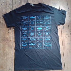May include: Black t-shirt with a blue graphic of a timeline of UFO sightings. The graphic includes the date, location, and a simple illustration of the UFO.