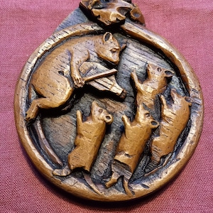 May include: A wooden carving of a bear playing a musical instrument with four smaller bears dancing around it. The carving is circular and has a brown wood finish.