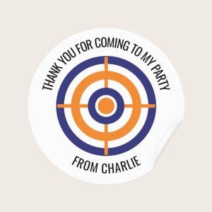 May include: A white, round sticker with a target design in blue and orange. The text "THANK YOU FOR COMING TO MY PARTY" arcs around the top, and "FROM CHARLIE" is at the bottom. The sticker has a slight peel.