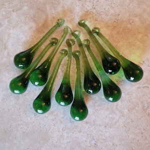 May include: A collection of nine teardrop-shaped glass ornaments in a translucent emerald green hue. Each piece features a smooth, elongated body that tapers to a rounded base and terminates in a small, circular loop at the top for hanging.