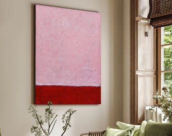May include: A living room scene featuring a large abstract painting with a pink upper section and a red lower section. The room includes a green sofa with pillows, a wooden coffee table, and a woven ottoman. A window with a bamboo shade is visible.