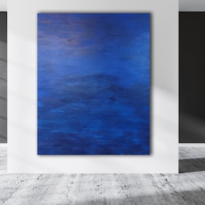 May include: An abstract painting with a deep blue color palette. The artwork is displayed on a white wall in a modern interior. The painting's texture and brushstrokes are visible, creating a sense of depth and movement. The room has a concrete floor and a large window.