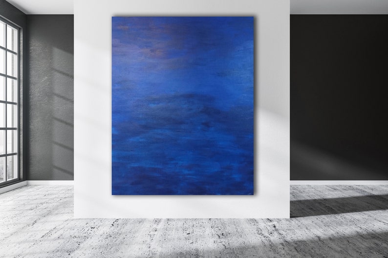 May include: An abstract painting with a deep blue color palette. The artwork is displayed on a white wall in a modern interior. The painting's texture and brushstrokes are visible, creating a sense of depth and movement. The room has a concrete floor and a large window.