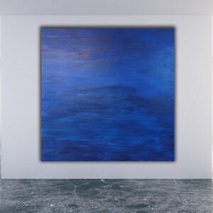 May include: Large square abstract painting with shades of blue and hints of gold. The artwork is displayed on a white wall in a modern room with large windows overlooking a cityscape.
