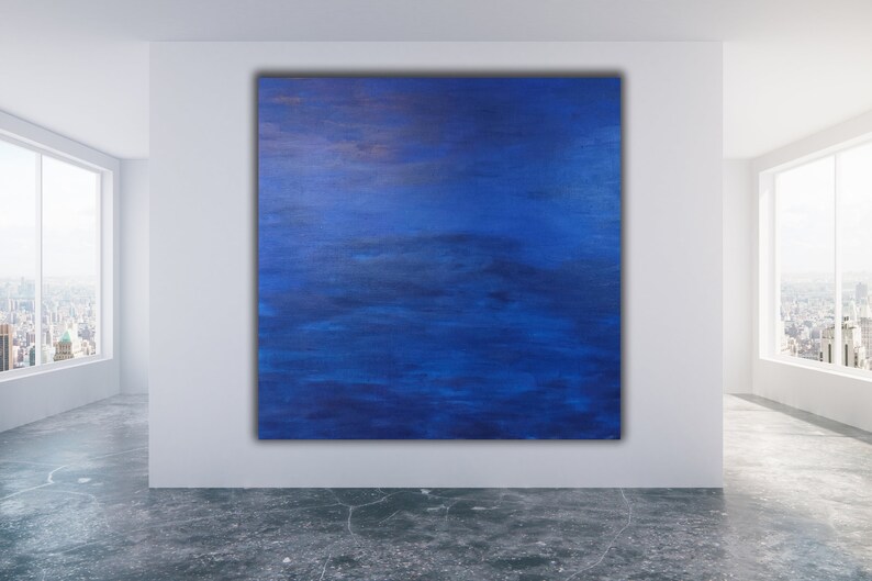 May include: Large square abstract painting with shades of blue and hints of gold. The artwork is displayed on a white wall in a modern room with large windows overlooking a cityscape.