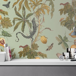 Puede incluir: Un papel tapiz verde con un patrón repetitivo de una planta tropical con fruta amarilla, un lagarto y varios insectos. El papel tapiz se muestra en un estante blanco con libros y artículos decorativos.