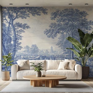 May include: A living room scene featuring a white sofa, a round wooden coffee table, and potted plants. The focal point is a blue and white mural depicting a landscape with trees, a bridge, and a distant town. The room has a modern, minimalist aesthetic.
