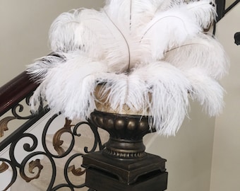 May include: A white ostrich feather arrangement in a brown ceramic vase on a black metal stand. The stand has a square base and a tall, slender pole.