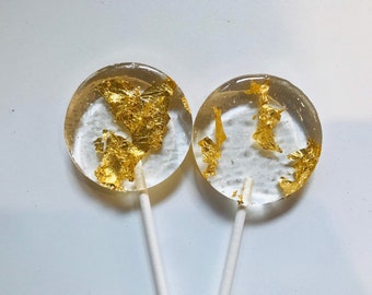 May include: Two round lollipops with gold leaf flakes embedded in the clear candy. The lollipops are on white sticks.
