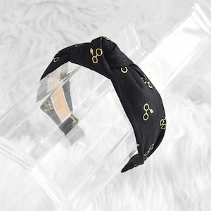 May include: Black knotted headband with a gold print of glasses and a lightning bolt.