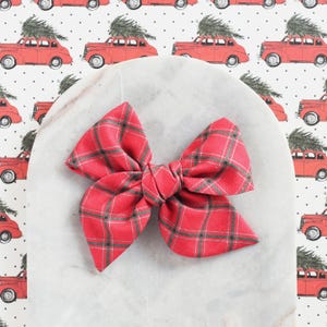 May include: A red and green plaid bow with a large, knotted center. The bow is on a white marble surface.