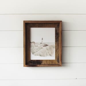 May include: A framed watercolor painting of a lighthouse on a sandy beach with tall grass in the foreground.